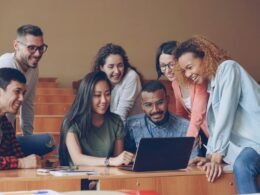 Mehrere Studierende mit unterschiedlichem Hintergrund diskutieren an einem Tisch zusammen vor einem Laptop
