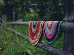Decke hängt an einem Holzzaun in einem Feld mit grasbewachsener Umgebung im Freien