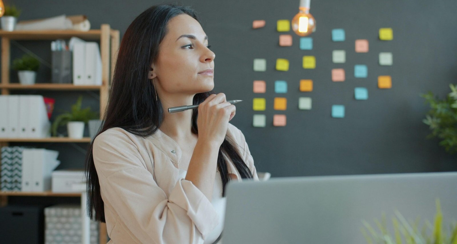 Frau sitzt nachdenklich an einem modernen Schreibtisch mit Stift in der Hand, alltägliche Büroszene