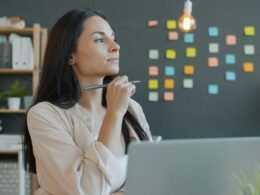 Frau sitzt nachdenklich an einem modernen Schreibtisch mit Stift in der Hand, alltägliche Büroszene
