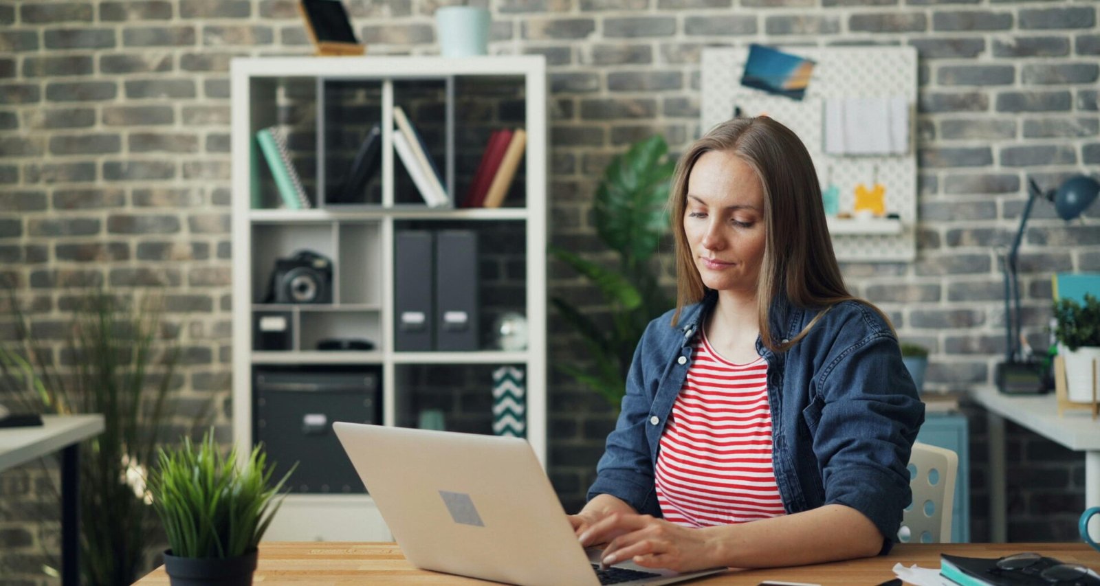 Eine Frau sitzt konzentriert an einem Schreibtisch und arbeitet an einem Laptop in einem modernen Büroraum.