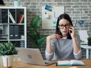 Eine Frau sitzt an einem modernen Schreibtisch und telefoniert mit dem Handy im Büro, Fokus auf berufliche Kommunikation