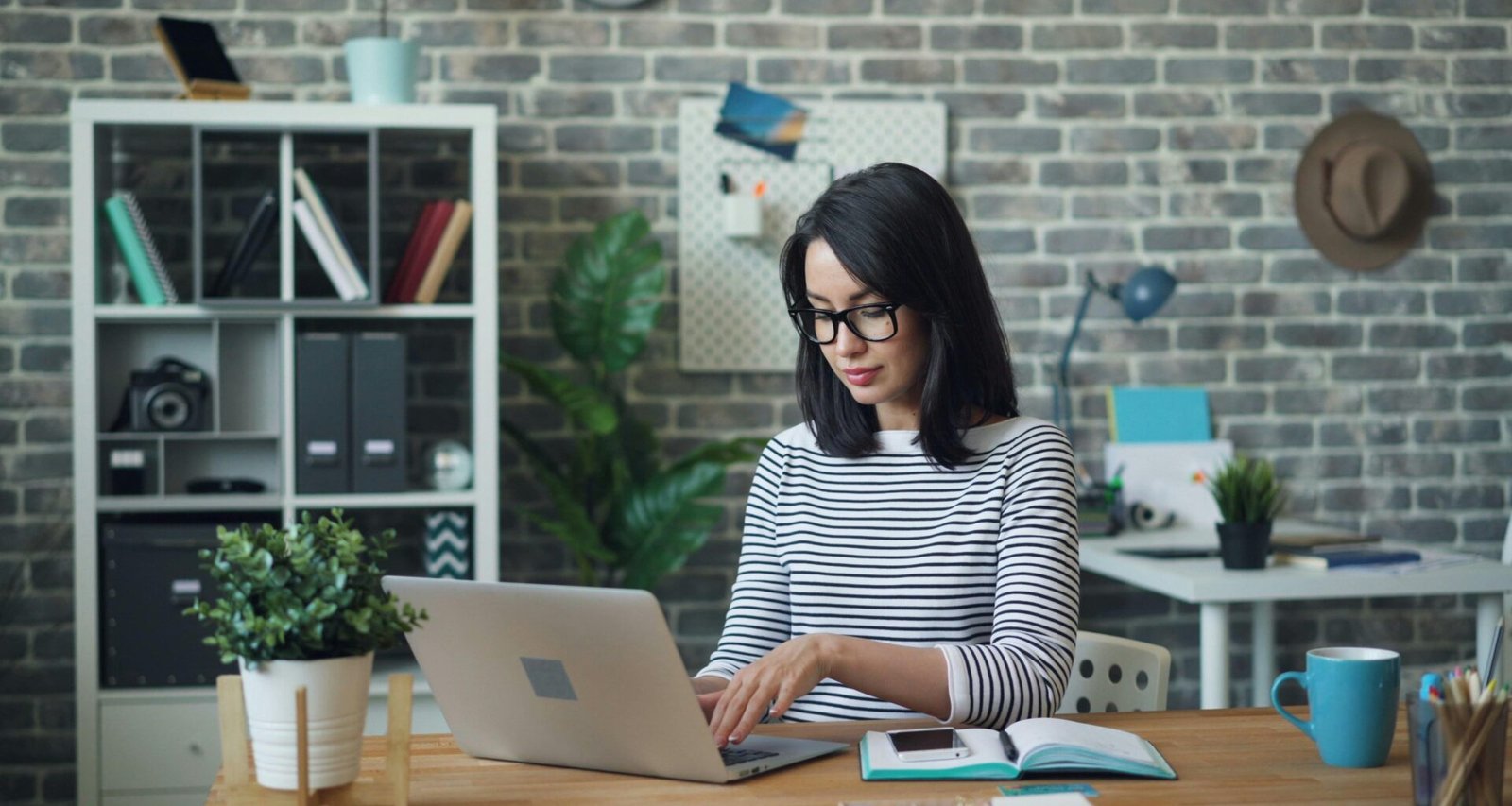Frau sitzt an einem Tisch und arbeitet an einem Laptop – Darstellung digitaler Arbeit im Alltag