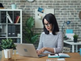 Frau sitzt an einem Tisch und arbeitet an einem Laptop – Darstellung digitaler Arbeit im Alltag