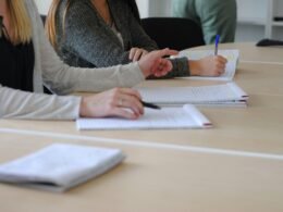 Frau sitzt am Tisch und schreibt auf einem Blatt Papier, um Aufgaben zu organisieren oder Notizen zu machen.