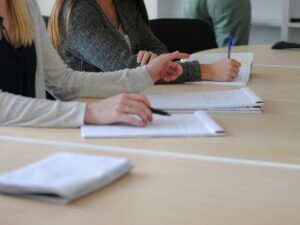 Frau sitzt am Tisch und schreibt auf einem Blatt Papier, um Aufgaben zu organisieren oder Notizen zu machen.
