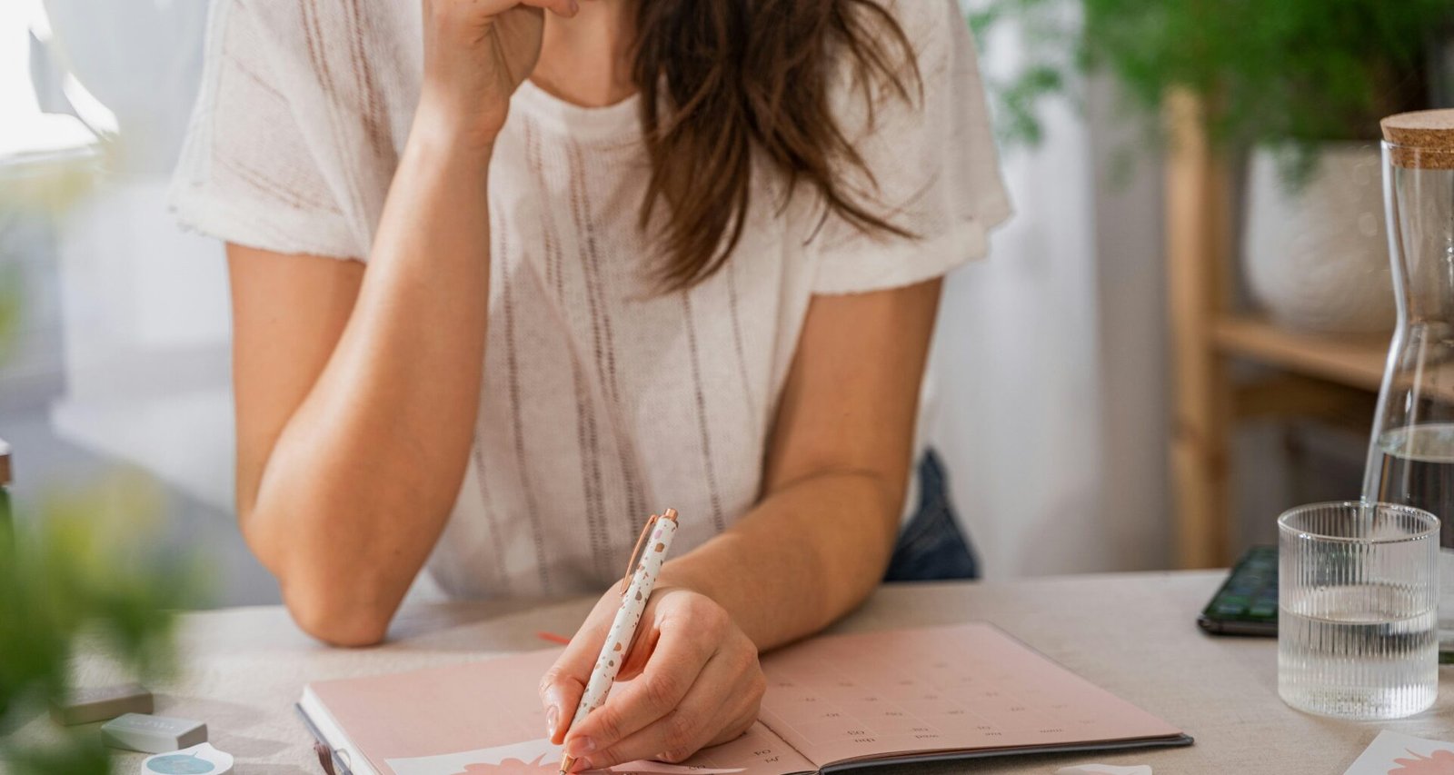 Eine Frau schreibt handschriftlich auf ein Blatt Papier an einem Tisch in einem hellen Raum