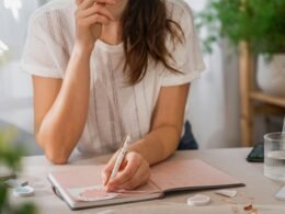 Eine Frau schreibt handschriftlich auf ein Blatt Papier an einem Tisch in einem hellen Raum