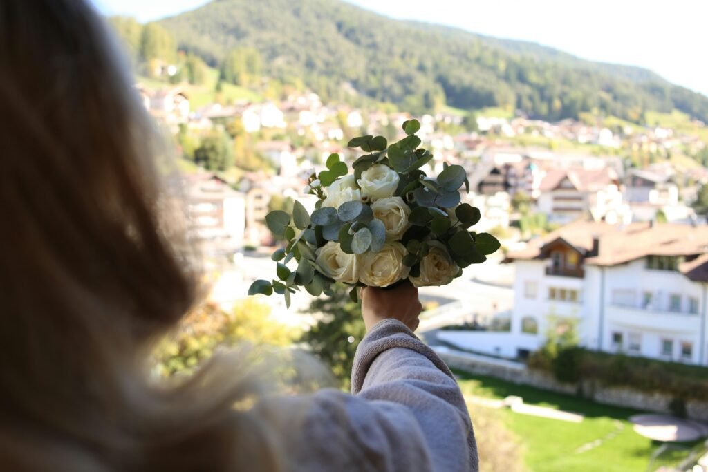 Eine Frau zeigt einen gemischten Blumenstrauß in der Hand, stehend vor neutralem Hintergrund im Tageslicht.