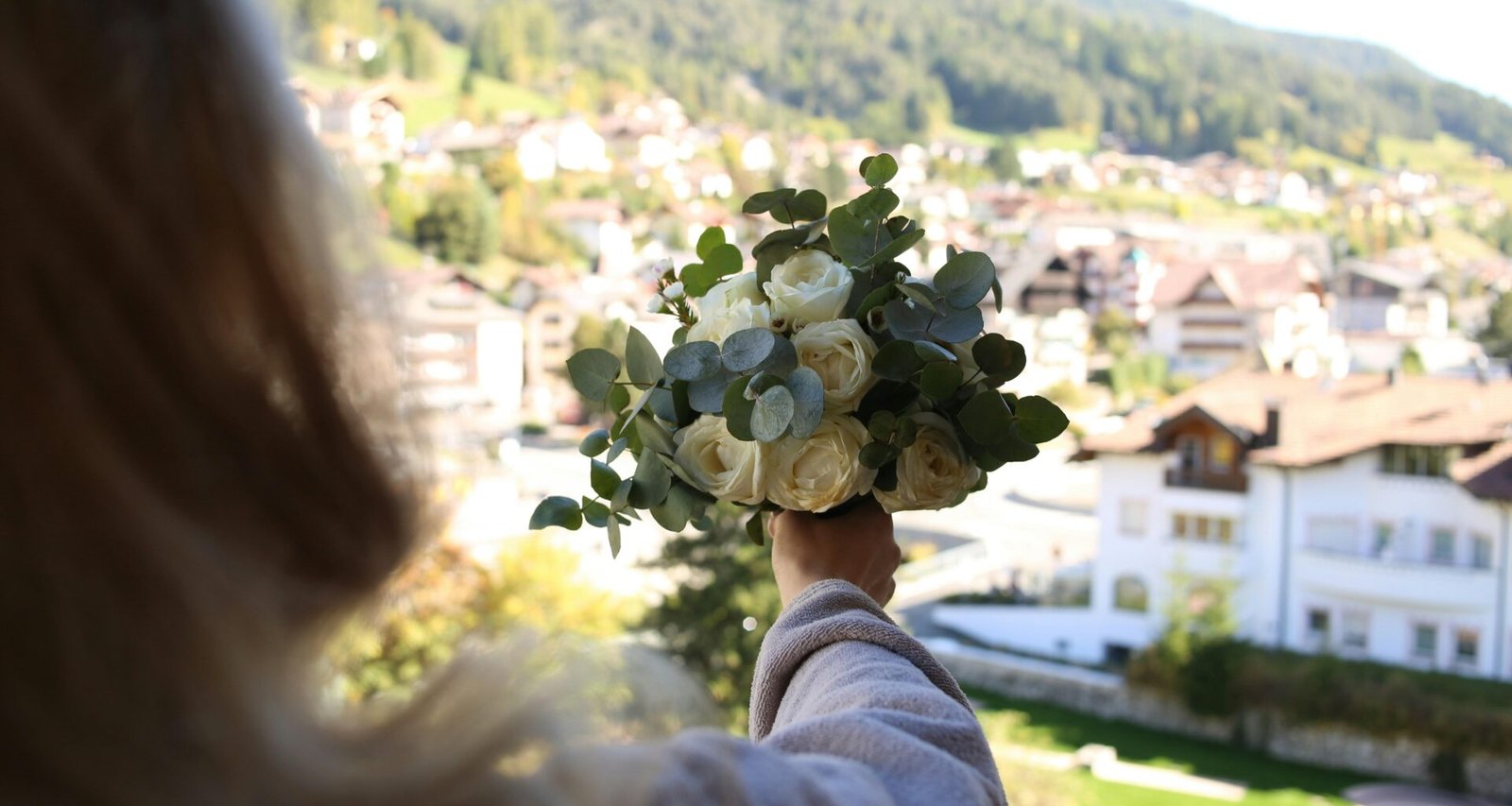 Eine Frau zeigt einen gemischten Blumenstrauß in der Hand, stehend vor neutralem Hintergrund im Tageslicht.