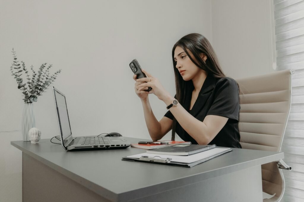 Frau sitzt an einem Schreibtisch und schaut auf ihr Smartphone in einem modernen Büro