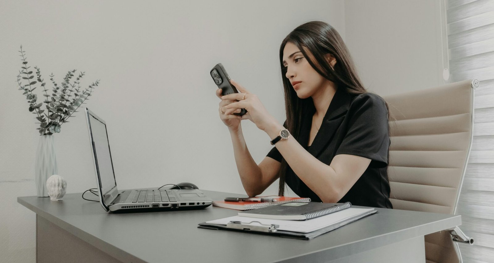 Frau sitzt an einem Schreibtisch und schaut auf ihr Smartphone in einem modernen Büro