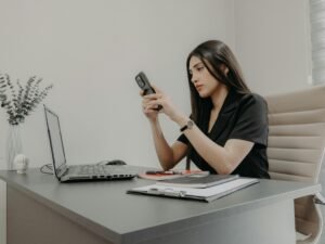 Frau sitzt an einem Schreibtisch und schaut auf ihr Smartphone in einem modernen Büro
