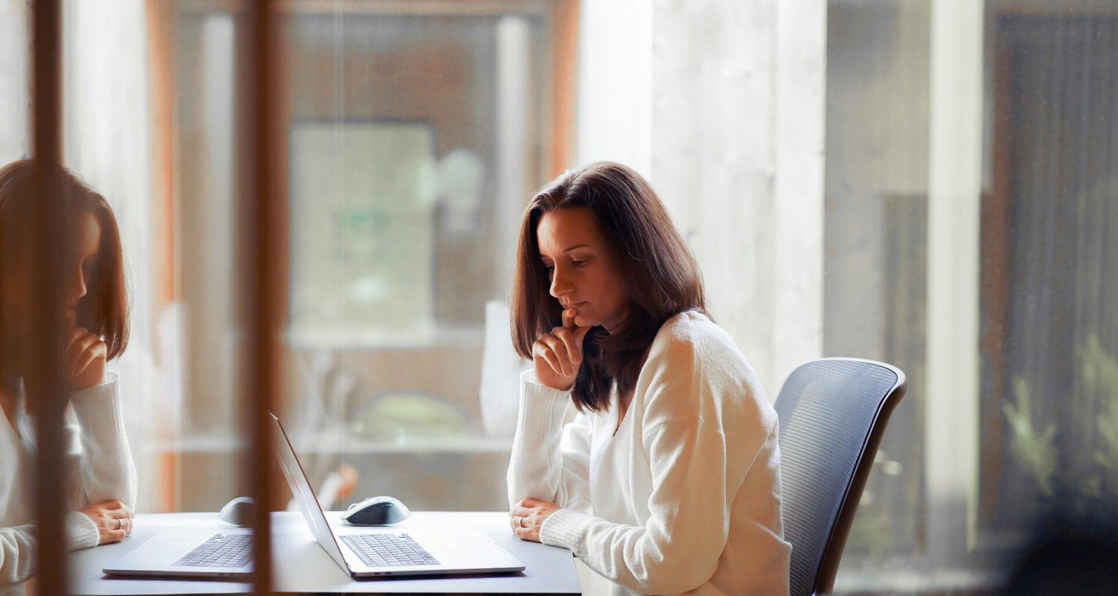 Eine Frau sitzt an einem Tisch und arbeitet an einem Laptop – Sinnbild für digitale Arbeitswelt und Homeoffice.