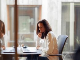 Eine Frau sitzt an einem Tisch und arbeitet an einem Laptop – Sinnbild für digitale Arbeitswelt und Homeoffice.