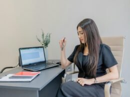 Frau im schwarzen Anzug arbeitet konzentriert an ihrem Schreibtisch mit Laptop und Notizbuch in einem modernen Büro