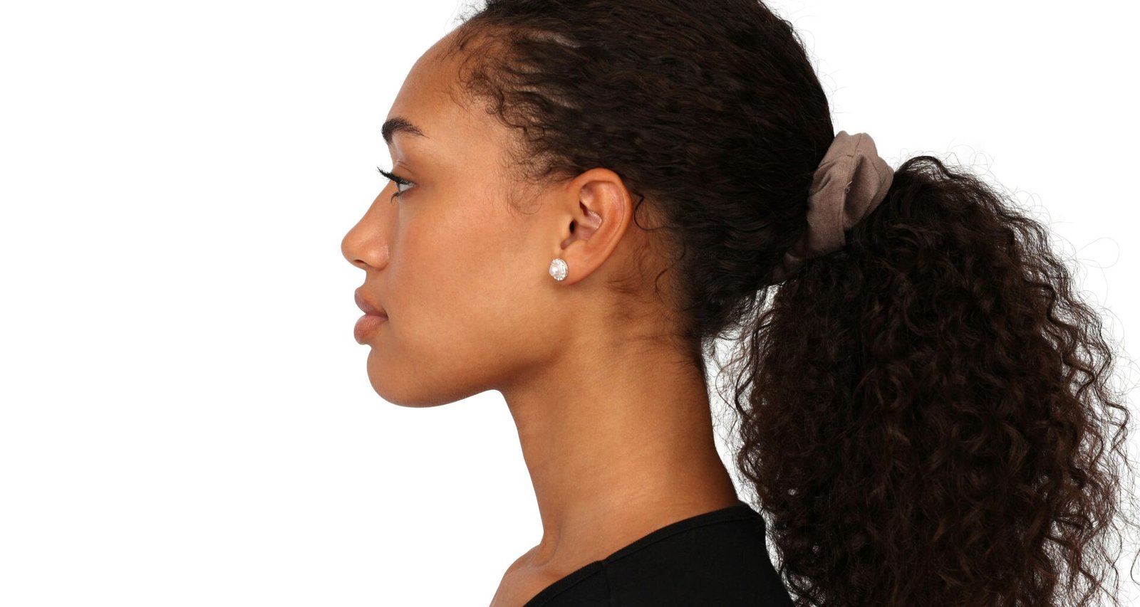 Eine Frau mit Ponytail sitzt entspannt und blickt nach vorn. Im Hintergrund ein neutraler, heller Raum.