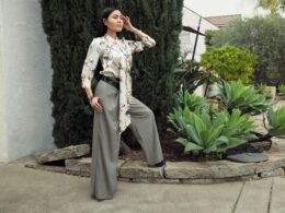 Frau trägt weite Hose und ein gemustertes Oberteil, steht vor neutralem Hintergrund, Mode und Kleidung im Detail sichtbar.