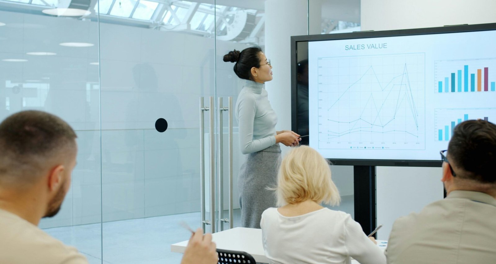 Frau zeigt Kollegen in einem modernen Büro Diagramme und Statistiken auf einem Bildschirm während einer Präsentation