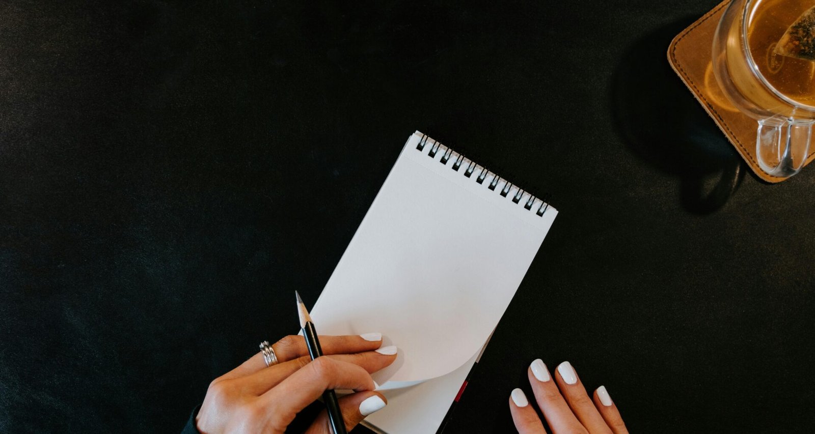 Frau macht handschriftliche Notizen in ein Notizbuch, daneben steht eine Tasse Kaffee auf dem Tisch