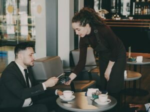 Eine Frau überreicht einem Mann eine Tasse Kaffee an einem Tisch in einem hellen Café mit freundlicher Atmosphäre.