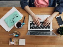 Frau sitzt an einem Tisch und arbeitet an einem Laptop, konzentriert im modernen Homeoffice-Umfeld