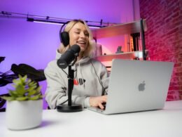 Eine Frau sitzt an einem Tisch vor einem aufgeklappten Laptop und arbeitet konzentriert an ihrem Computer.