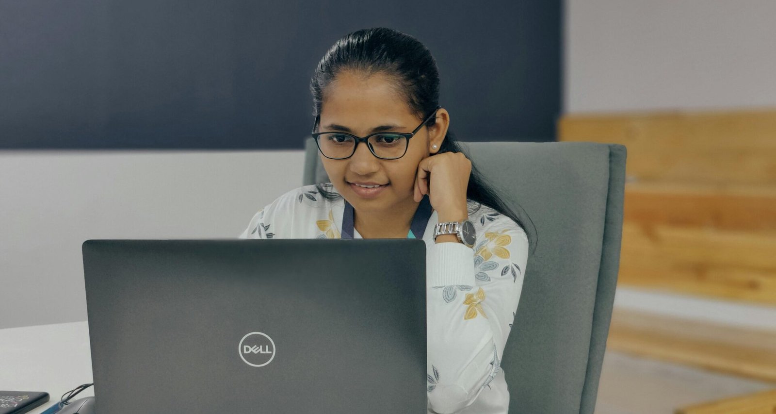 Eine Frau sitzt zu Hause an einem Tisch und arbeitet mit einem Laptop, Fokus auf die Arbeitsumgebung