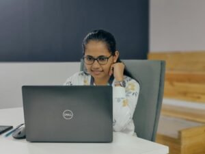 Eine Frau sitzt zu Hause an einem Tisch und arbeitet mit einem Laptop, Fokus auf die Arbeitsumgebung