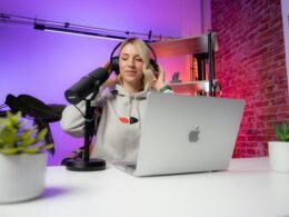 Eine Frau sitzt in einem modernen Raum vor einem aufgeklappten Laptop und arbeitet konzentriert am Bildschirm