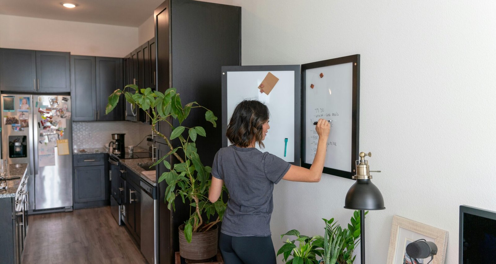 Eine Frau steht in einer modernen Küche vor einem Kühlschrank und betrachtet den Inhalt.