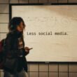 Frau vor einem Schild mit der Aufschrift 'less social media', im Kontext bewusster Social-Media-Nutzung dargestellt
