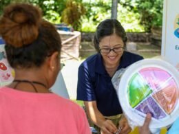 Eine Frau hält einen farbenfrohen Teller mit verschiedenen Lebensmitteln einer weiteren Person entgegen.
