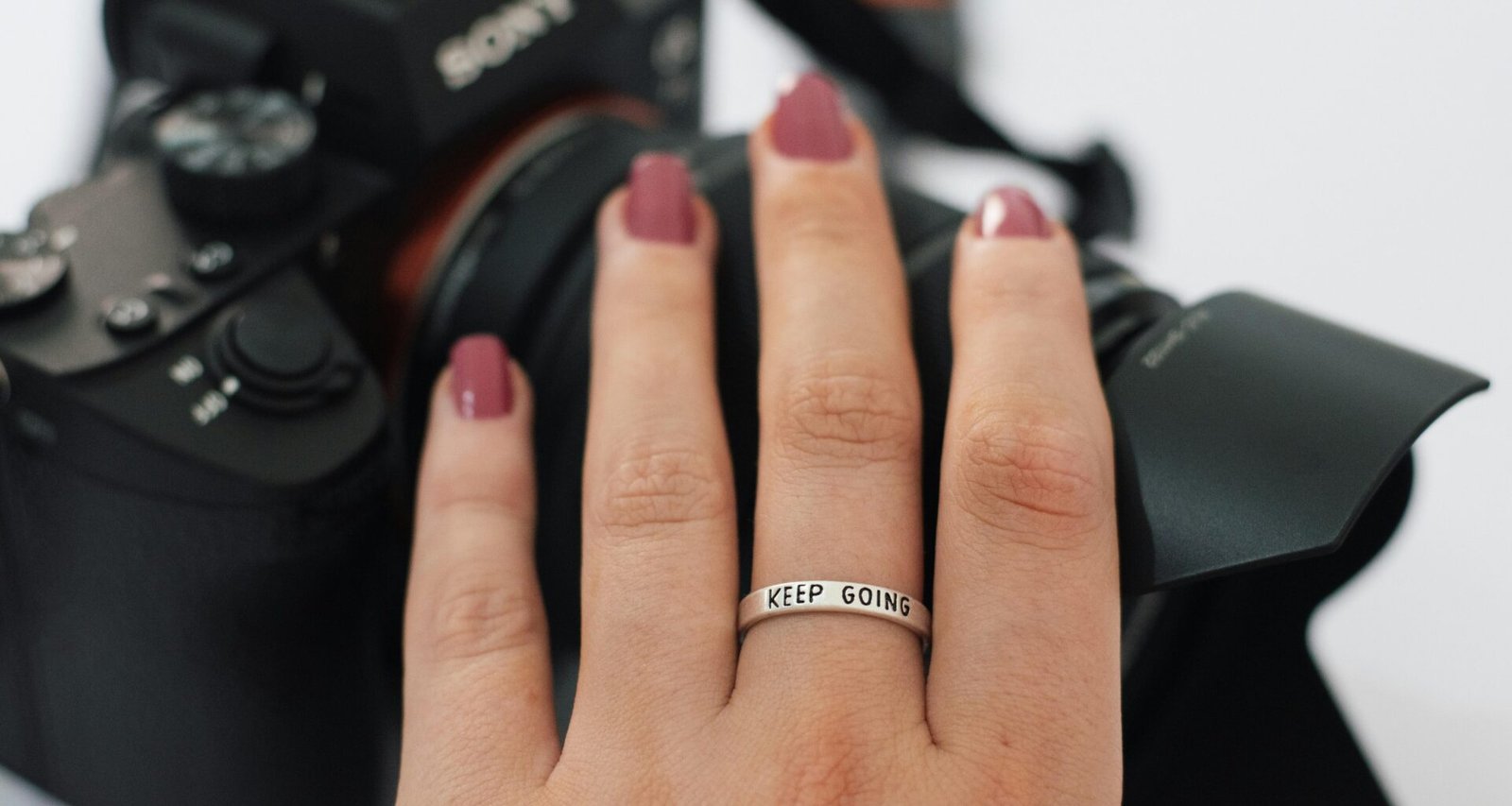 Nahaufnahme einer Frauenhand mit Ring, die eine Kamera am Handgelenk hält, ideal für Technik- und Lifestyle-Themen.