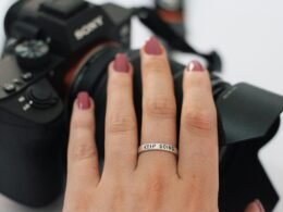 Nahaufnahme einer Frauenhand mit Ring, die eine Kamera am Handgelenk hält, ideal für Technik- und Lifestyle-Themen.