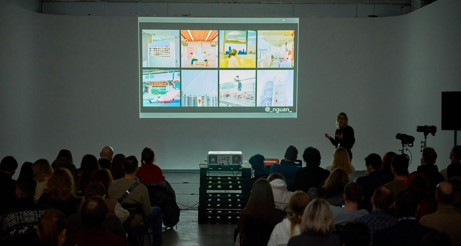 Viele Personen sitzen dicht beieinander in einem modernen, hellen Raum und nehmen an einer Veranstaltung teil.