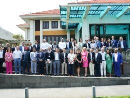 Große Menschengruppe steht gesammelt im Außenbereich vor einem modernen Gebäudeeingang, Tageslicht, urbanes Umfeld