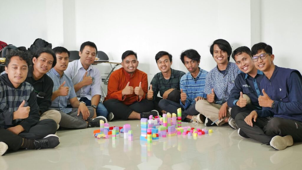 Mehrere Männer sitzen nebeneinander und arbeiten gemeinsam an einem Tisch. Gespräch und Koordination stehen im Vordergrund.