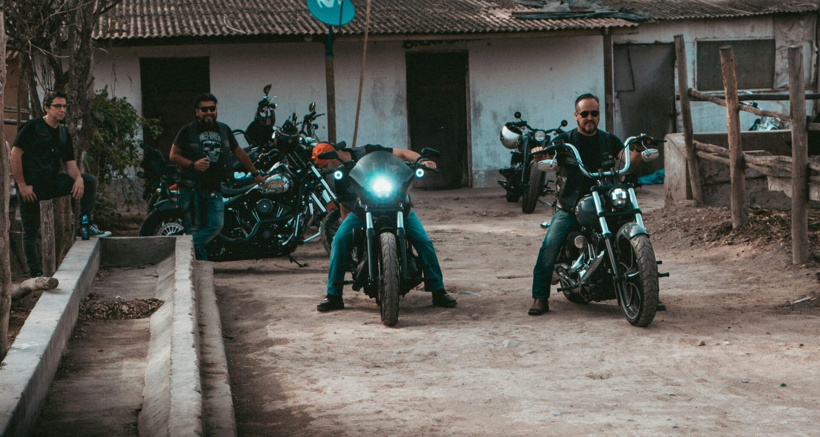 Mehrere Männer fahren mit Motorrädern gemeinsam eine unbefestigte Schotterstraße entlang, Staub wirbelt auf