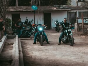 Mehrere Männer fahren mit Motorrädern gemeinsam eine unbefestigte Schotterstraße entlang, Staub wirbelt auf