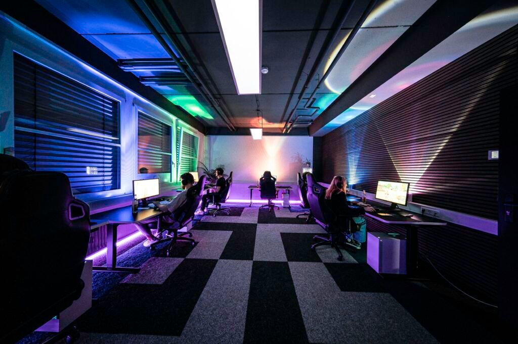 Mehrere Personen sitzen in einem hellen Raum an Schreibtischen und arbeiten gemeinsam am Computer.