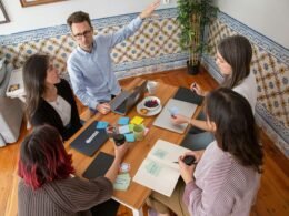Mehrere Personen sitzen bei einem Teammeeting um einen großen Holztisch und arbeiten gemeinsam an Ideen.