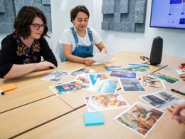 Mehrere Personen sitzen um einen rechteckigen Holztisch und arbeiten gemeinsam an Laptops und Notizbüchern.