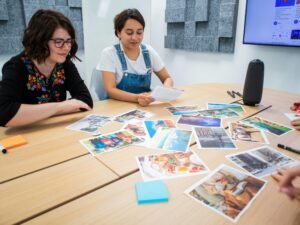 Mehrere Personen sitzen um einen rechteckigen Holztisch und arbeiten gemeinsam an Laptops und Notizbüchern.
