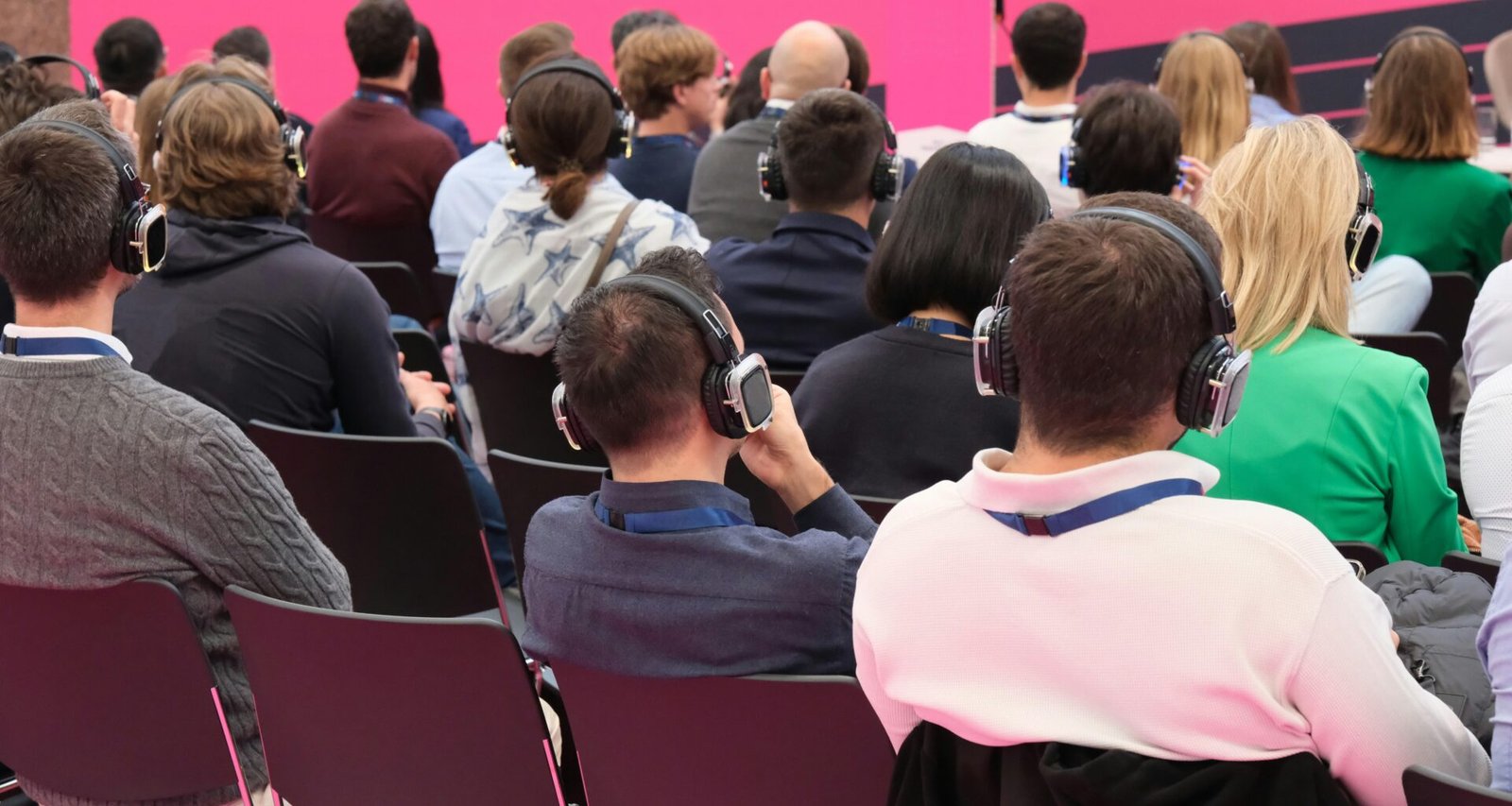 Eine Gruppe von Menschen sitzt vor einer pinken Wand, spricht zusammen und arbeitet an gemeinsamen Projekten.