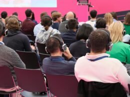 Eine Gruppe von Menschen sitzt vor einer pinken Wand, spricht zusammen und arbeitet an gemeinsamen Projekten.