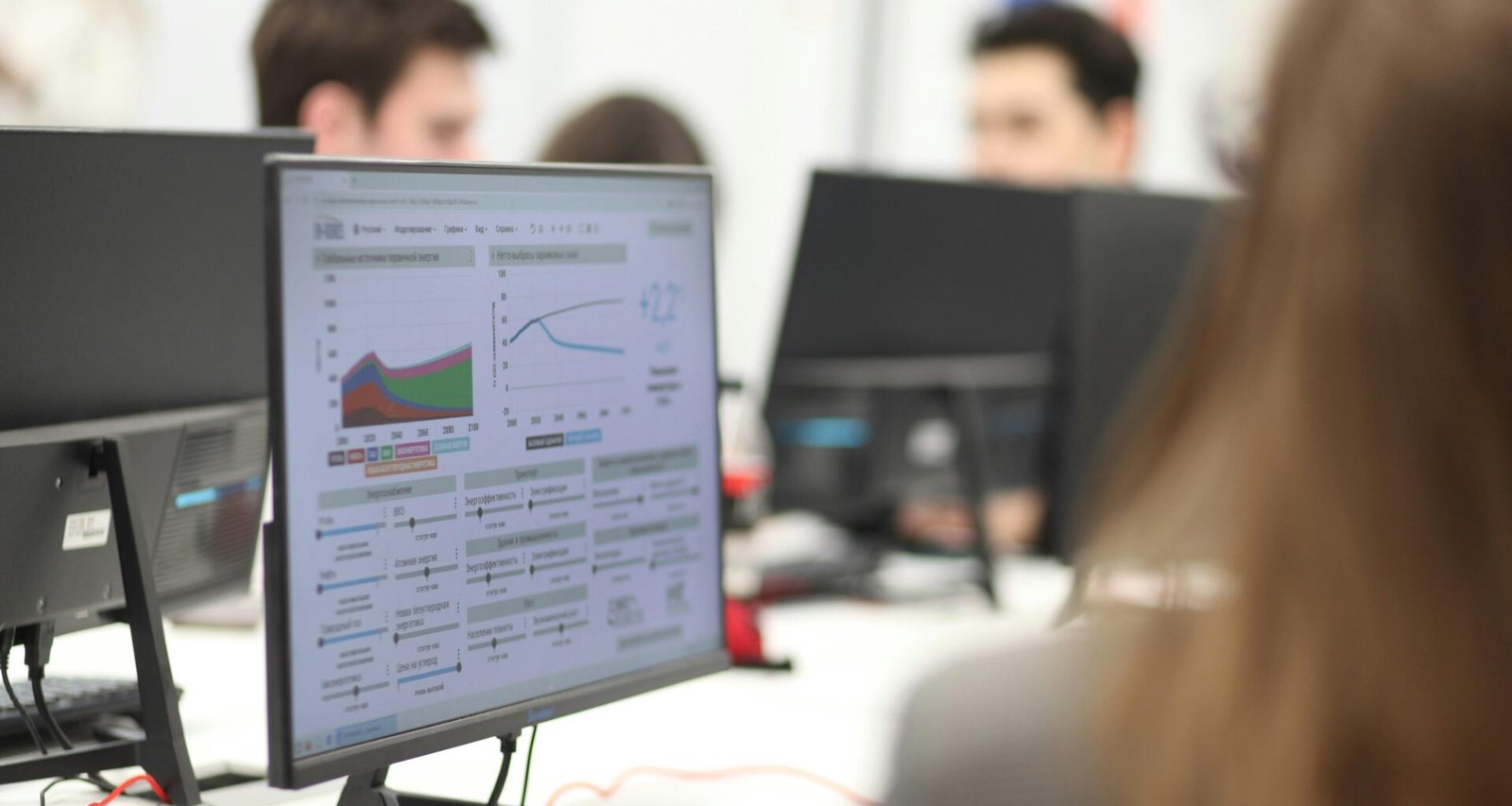 Mehrere Personen sitzen gemeinsam in einem Raum an Computern und arbeiten konzentriert an verschiedenen Aufgaben.