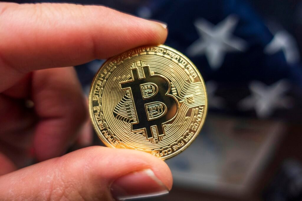 Hand hält eine Bitcoin-Münze vor einer amerikanischen Flagge, Symbol für Kryptowährungen und ihren Einfluss in den USA