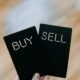 Hand hält zwei schwarze Karten mit den Aufschriften Buy und Sell, Symbol für Kauf- und Verkaufsvorgänge