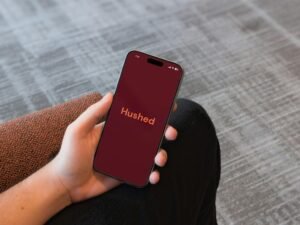 Hand mit Smartphone zeigt die Hushed-App auf dem Display, Fokus auf mobile Kommunikation und Datenschutz mit moderner Technologie.